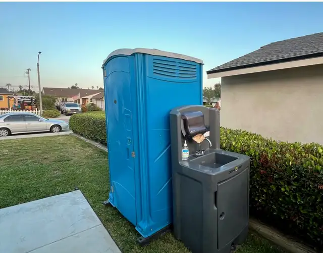 Blue porta potty with a handwashing station beside a home